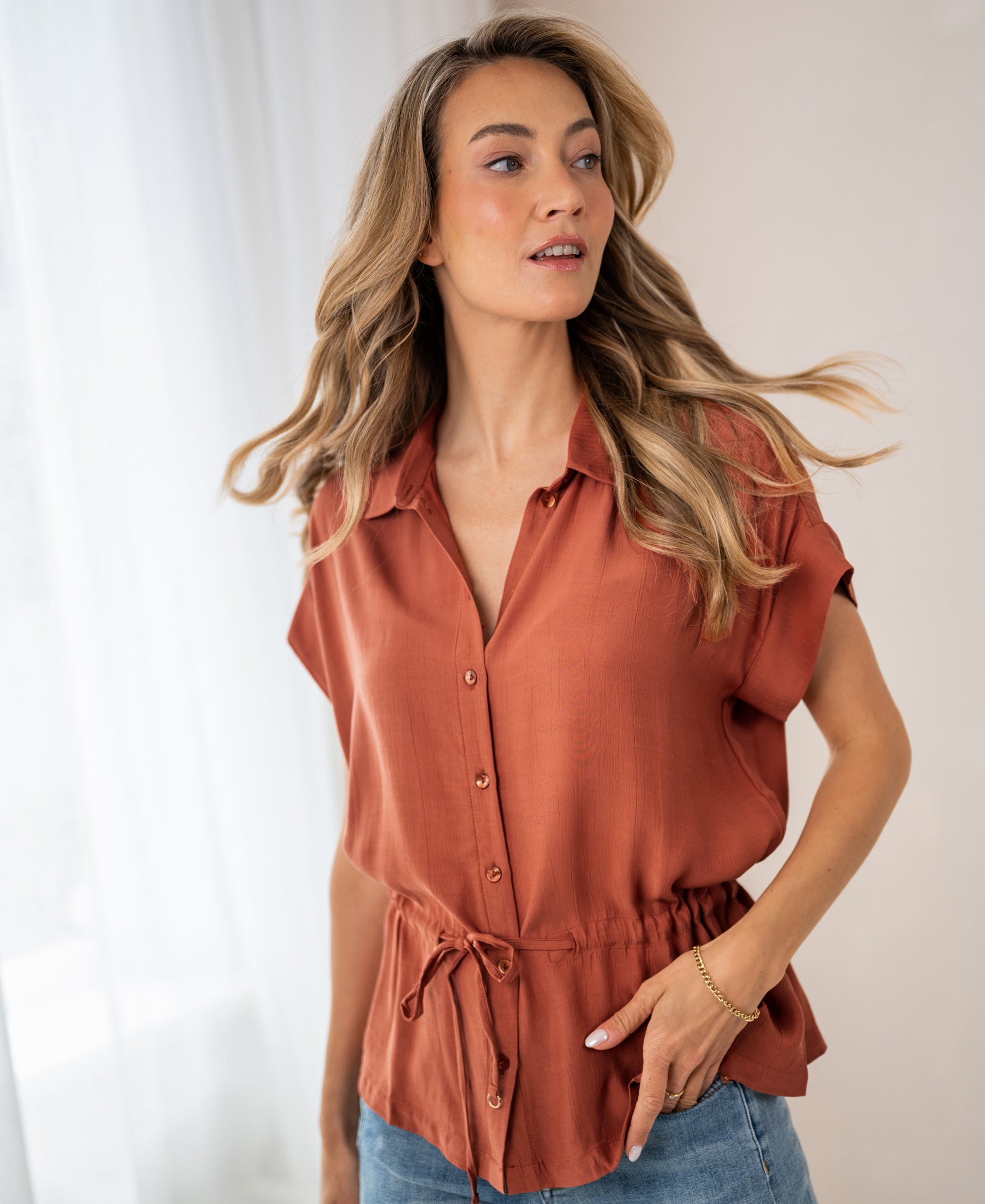 Woman wears a terra-colored Plein Publique blouse called La Jody.