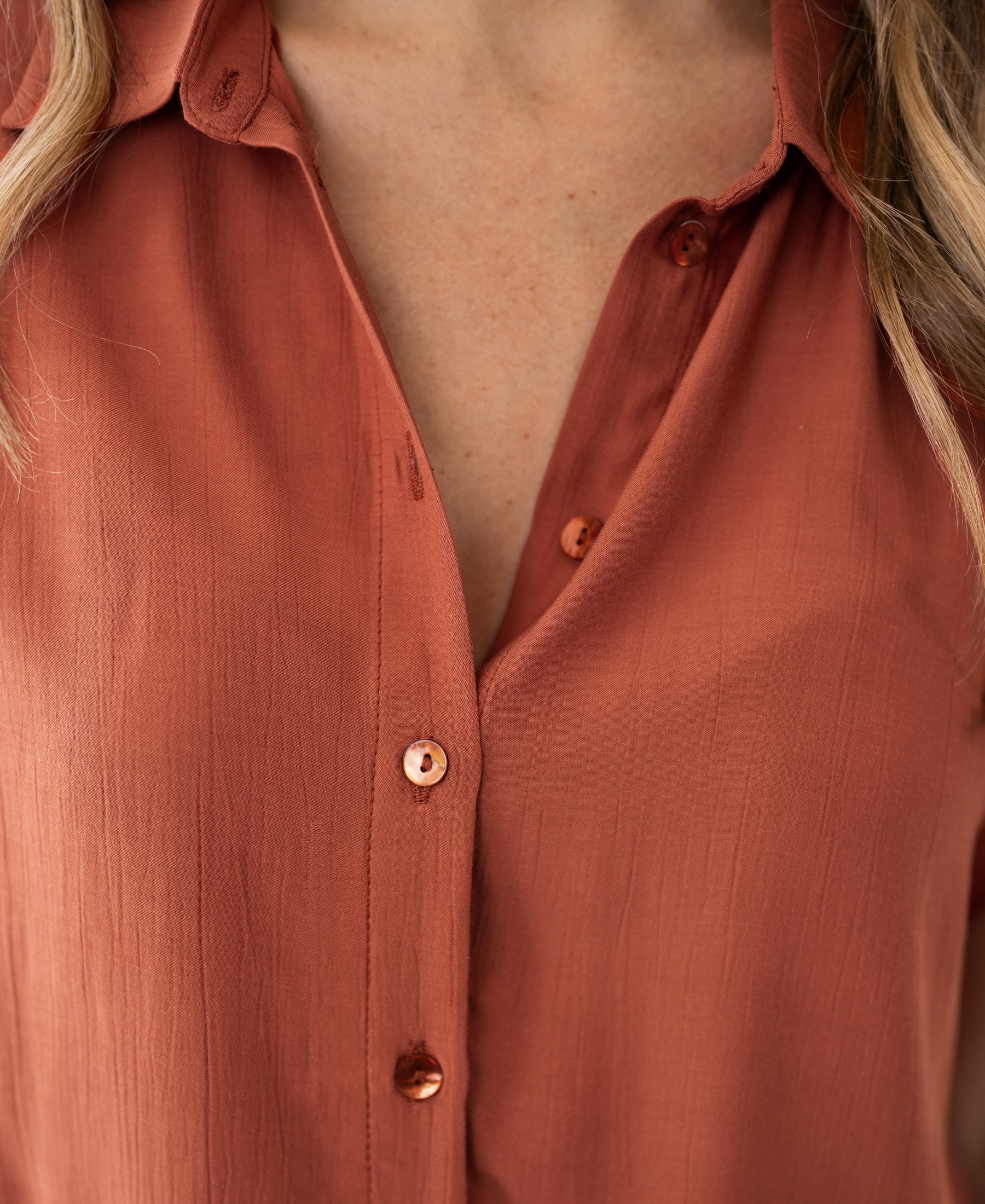Close-up of a soft viscose terra-colored blouse with loose fit, shown on a person with loose waves framing the face.