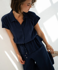 Navy blue PLEIN PUBLIQUE LA JODY blouse displayed on woman standing by a white wall, holding a glittery shoe.