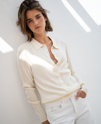 Woman wearing a cream Tencel-silk ribbed cardigan stands by a white wall, facing the camera.