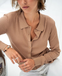A woman wears the Tencel-silk ribbed cardigan in sand, her hand resting on her knee.