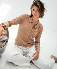 Woman wears a sand-colored Tencel-silk ribbed vest, seated on a white floor.