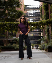 Woman wearing plum Merino wool collared top, seen outdoors on a city walkway.