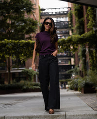 Plum merino wool collared top shown outdoors among greenery and brick buildings.