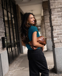 Woman wearing a dark teal merino wool top stands by brick columns.