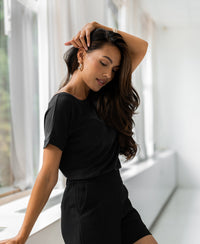 Charcoal gray two-way T-shirt in soft fabric, shown worn by a woman standing by a window in natural light.