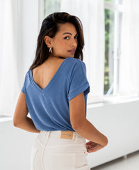 Woman with long dark hair wears the PLEIN PUBLIQUE Two-way T-shirt LA JULIEN in jeans blue, looking over her shoulder.