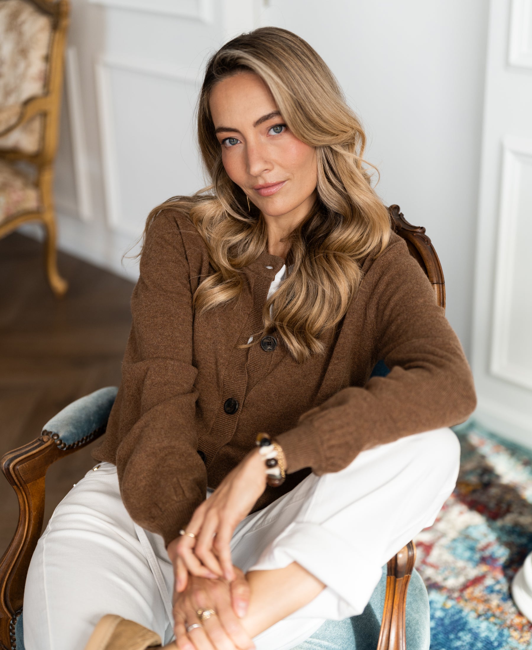 Woman wearing a tobacco-colored round-neck vest from PLEIN PUBLIQUE, seated on a chair.
