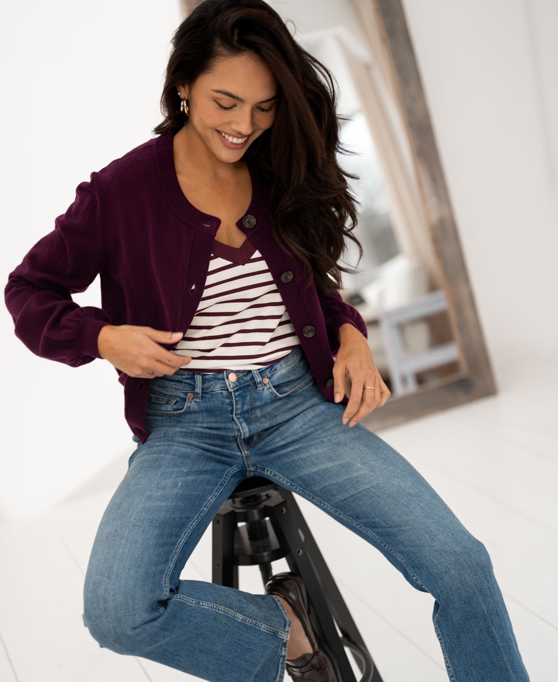 Woman wearing a round-neck dark cassis striped vest sits on a black stool.