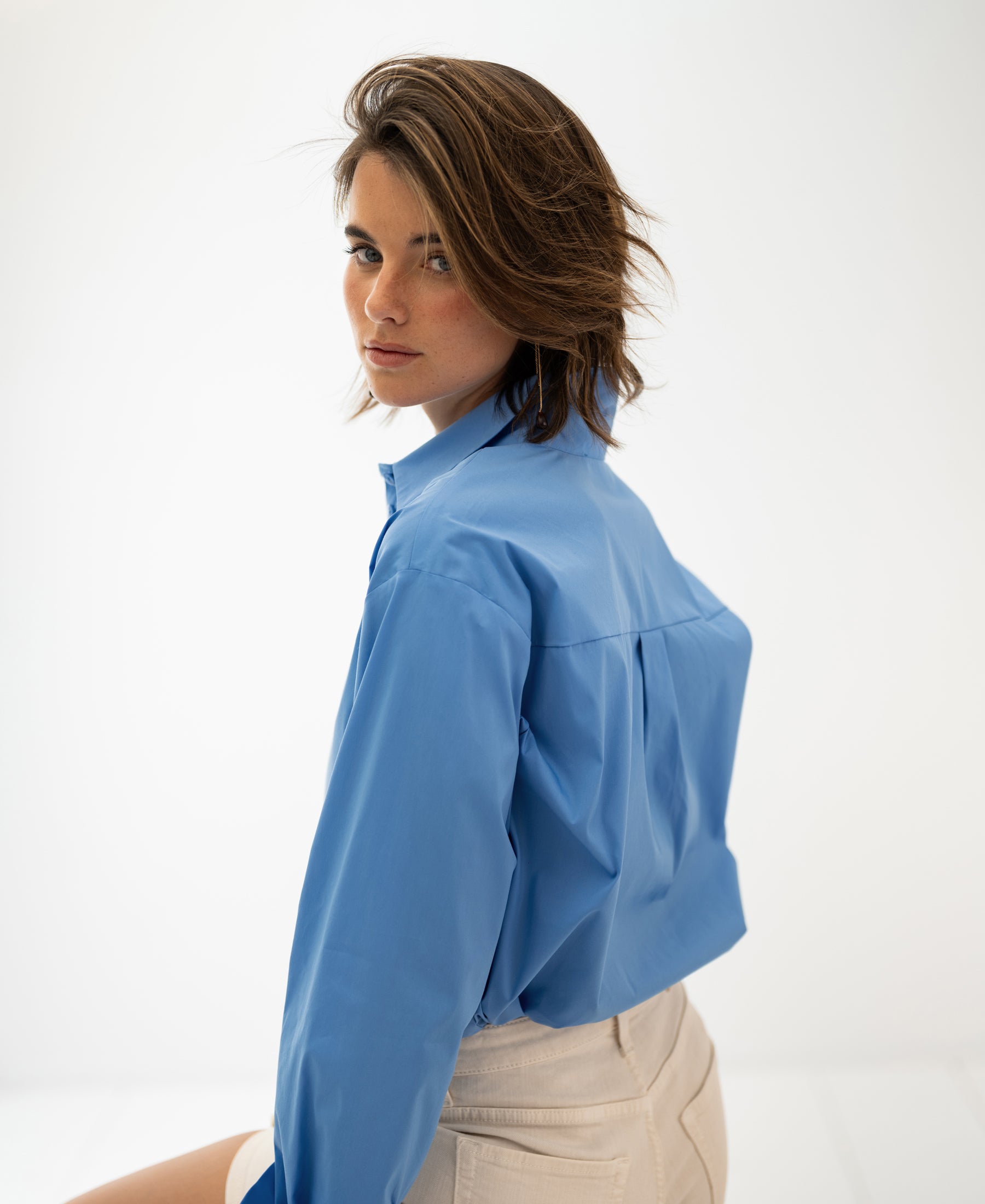 Oversized easy-iron blue blouse, shown from the back as the wearer looks over their shoulder.