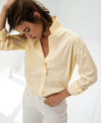 Oversized easy-iron blouse in soft yellow, shown on a woman standing in a bright, minimal space.