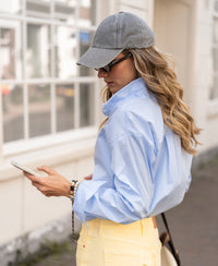 Oversized light blue checked blouse LE LILLE shown on a woman walking by a white building.