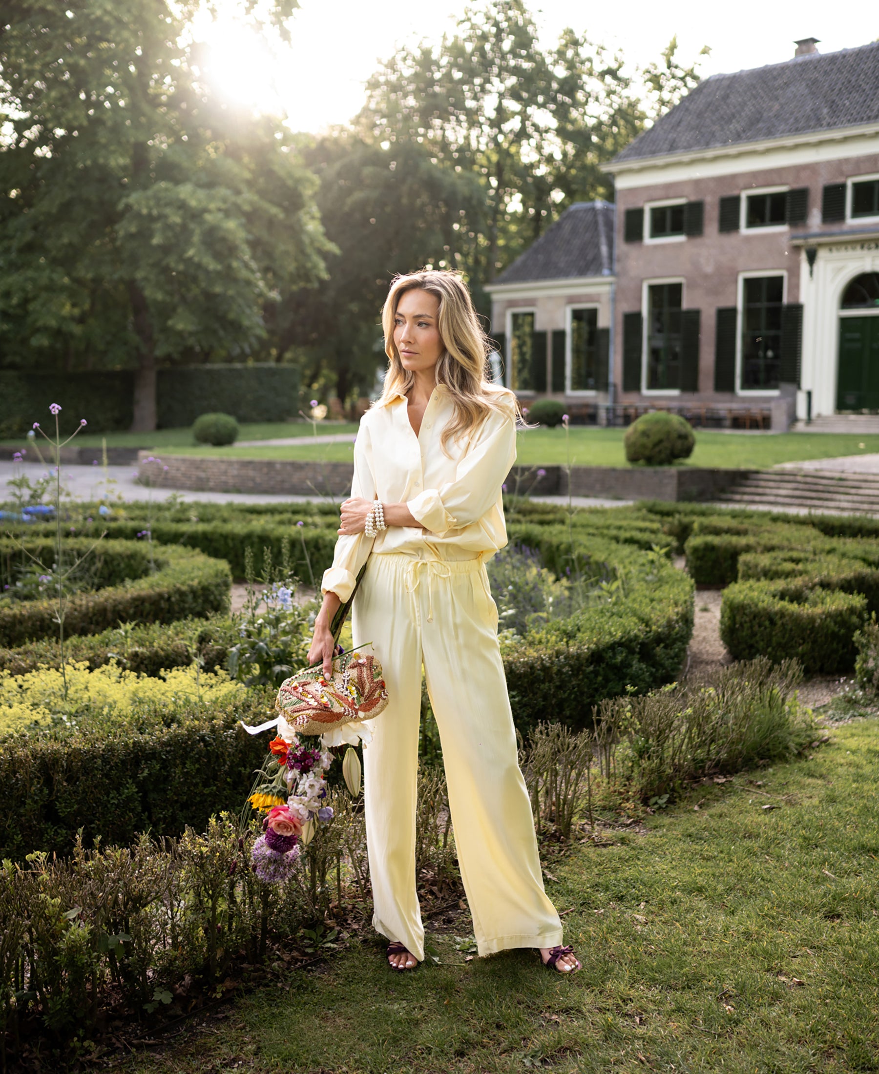 Oversized easy-iron soft yellow blouse displayed in a garden at sunset.