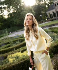 Oversized easy-iron blouse in soft yellow, shown outdoors in a sunlit garden.