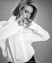 Black and white photo of the Plein Publique oversized white blouse, with model buttoning the front, seen from above.