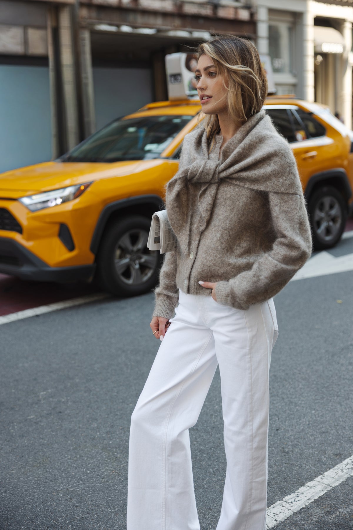 Woman wearing a beige mohair vest stands by a taxi.