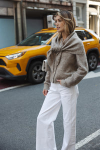 Woman wearing a beige mohair vest stands by a taxi.