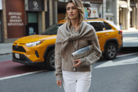 Woman wearing a sand-colored mohair scarf walks outside, city street in background.