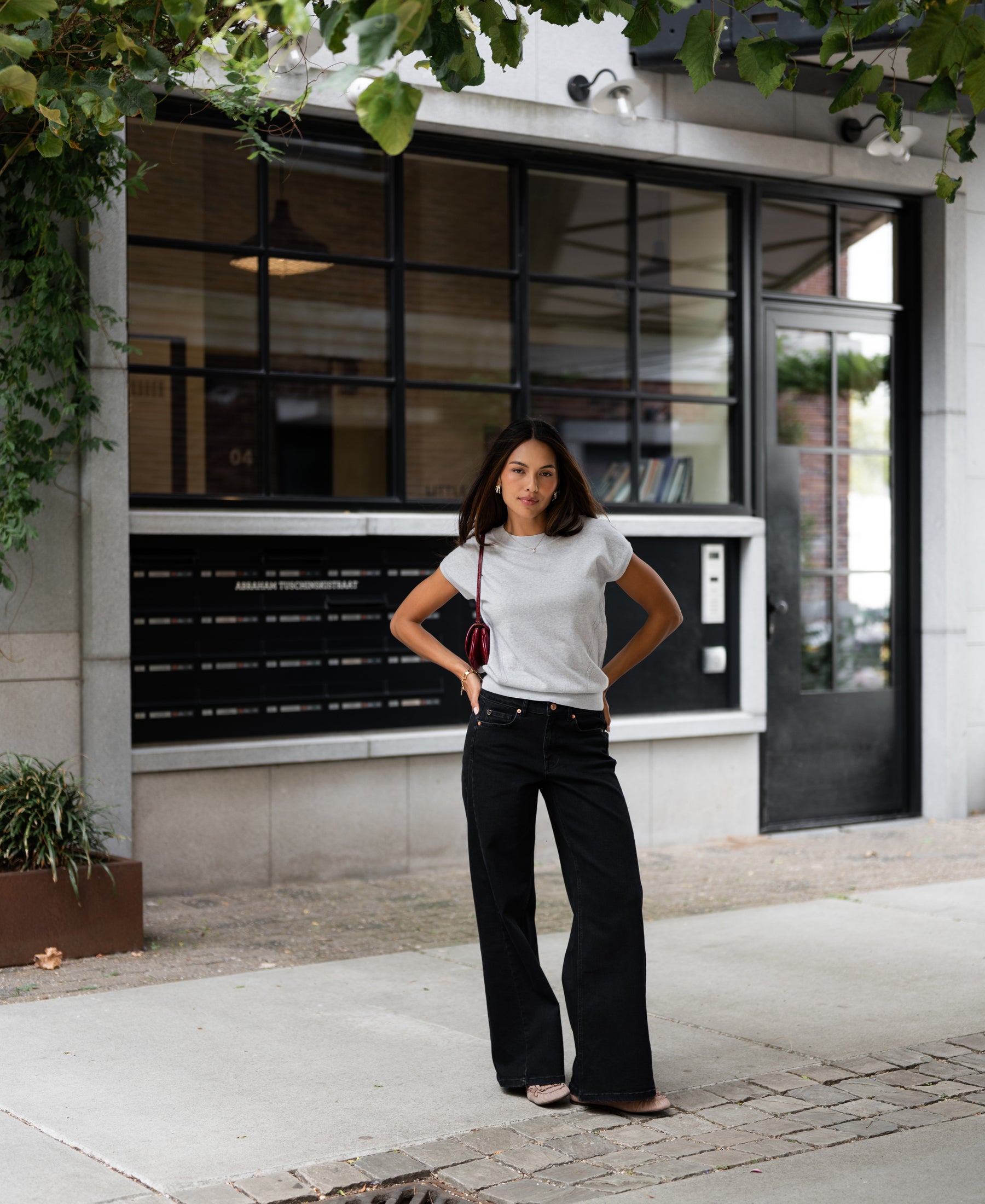 Woman wearing LE LOUIS silver-grey merino top standing outside in front of a modern building with large windows.