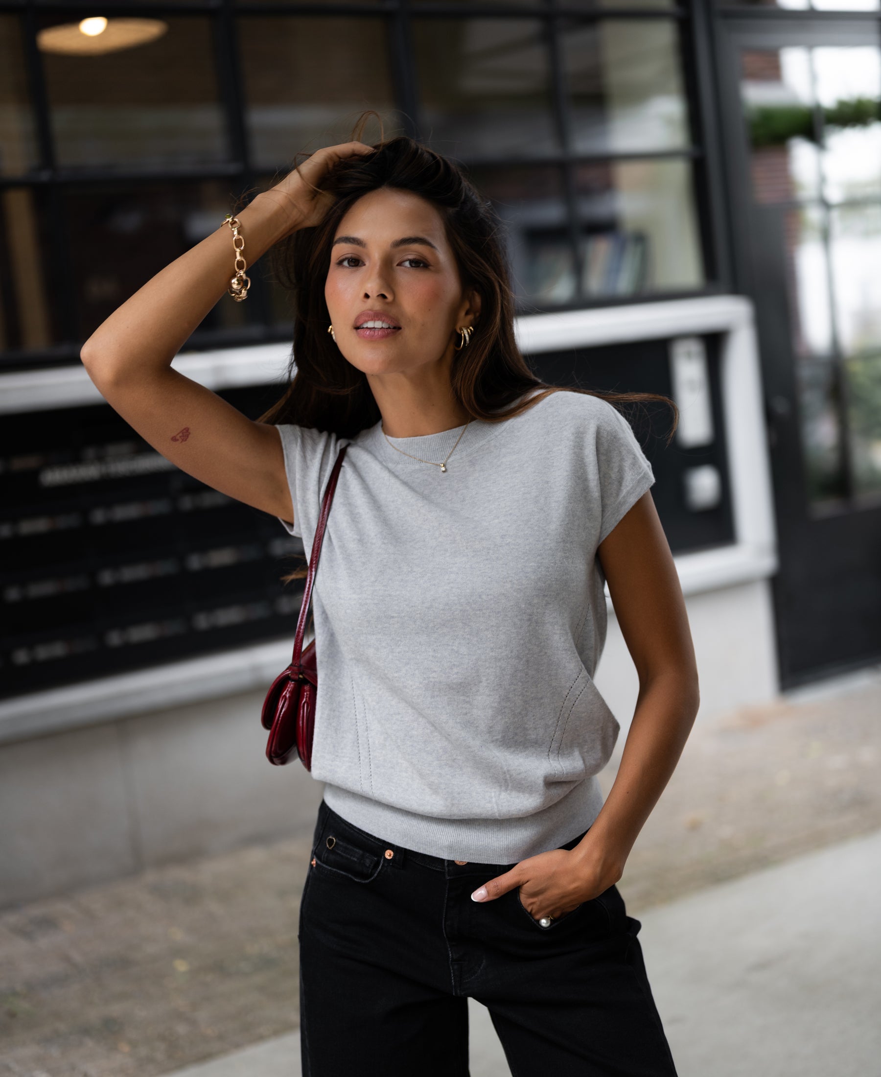 Woman wearing a Merino wool top in silver gray stands by a building with large windows.