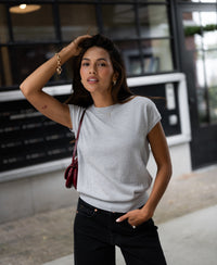 Woman wearing a Merino wool top in silver gray stands by a building with large windows.