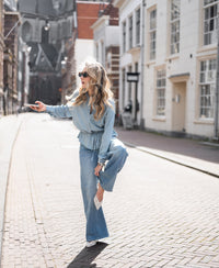 Woman wearing a bleached Tencel denim blouse adjusts her shoe outdoors on a sunny city street.