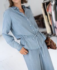 Woman wearing bleached Tencel denim blouse, standing with clothes displayed in the background.