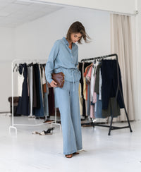 Woman wearing a bleached Tencel denim blouse stands in a studio with clothing racks in the background.