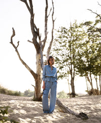 Woman wears light blue Tencel denim jeans on sandy ground near a tall, leafless tree.