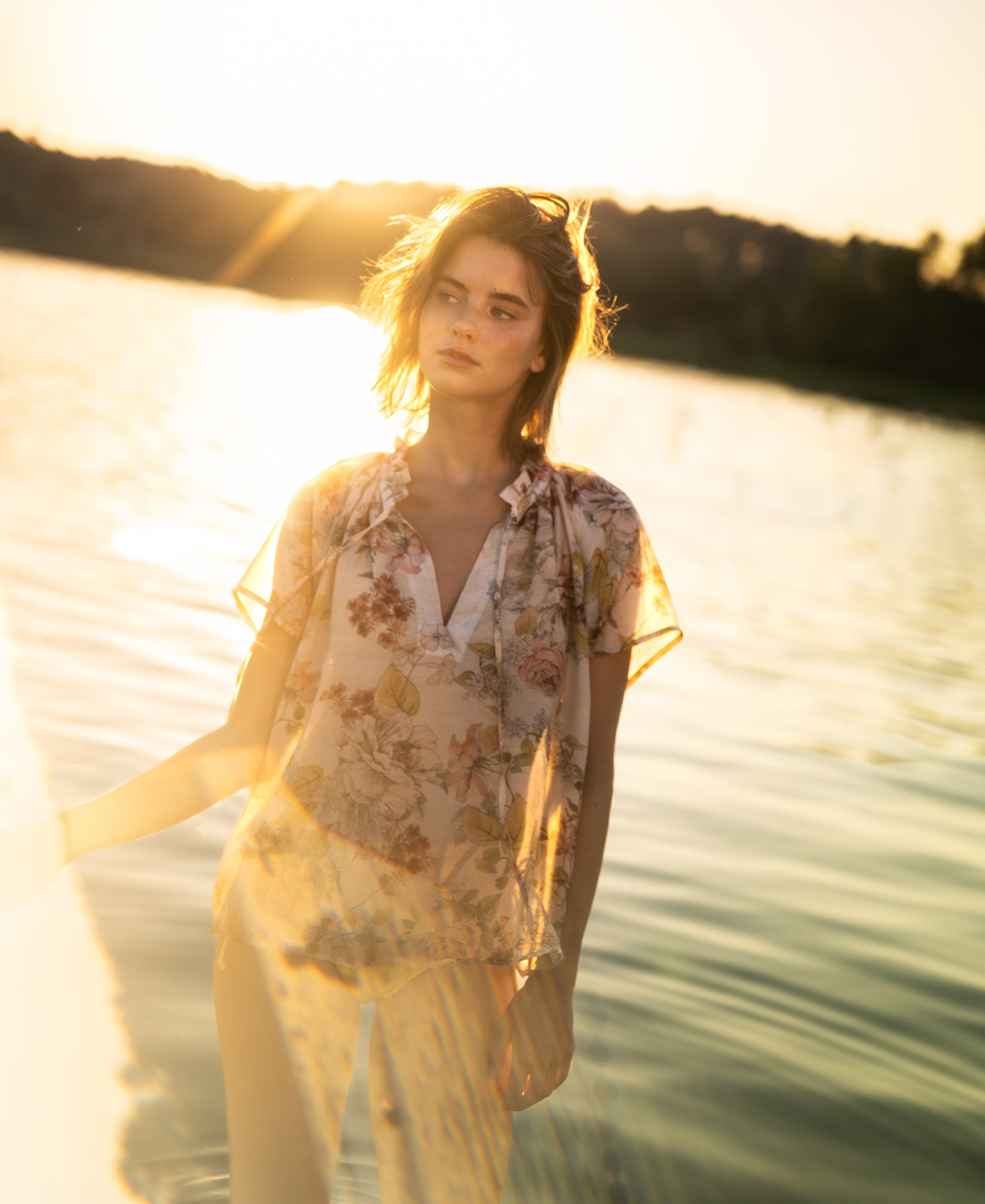 Blush floral print blouse top in size S shown by a lake at sunset.