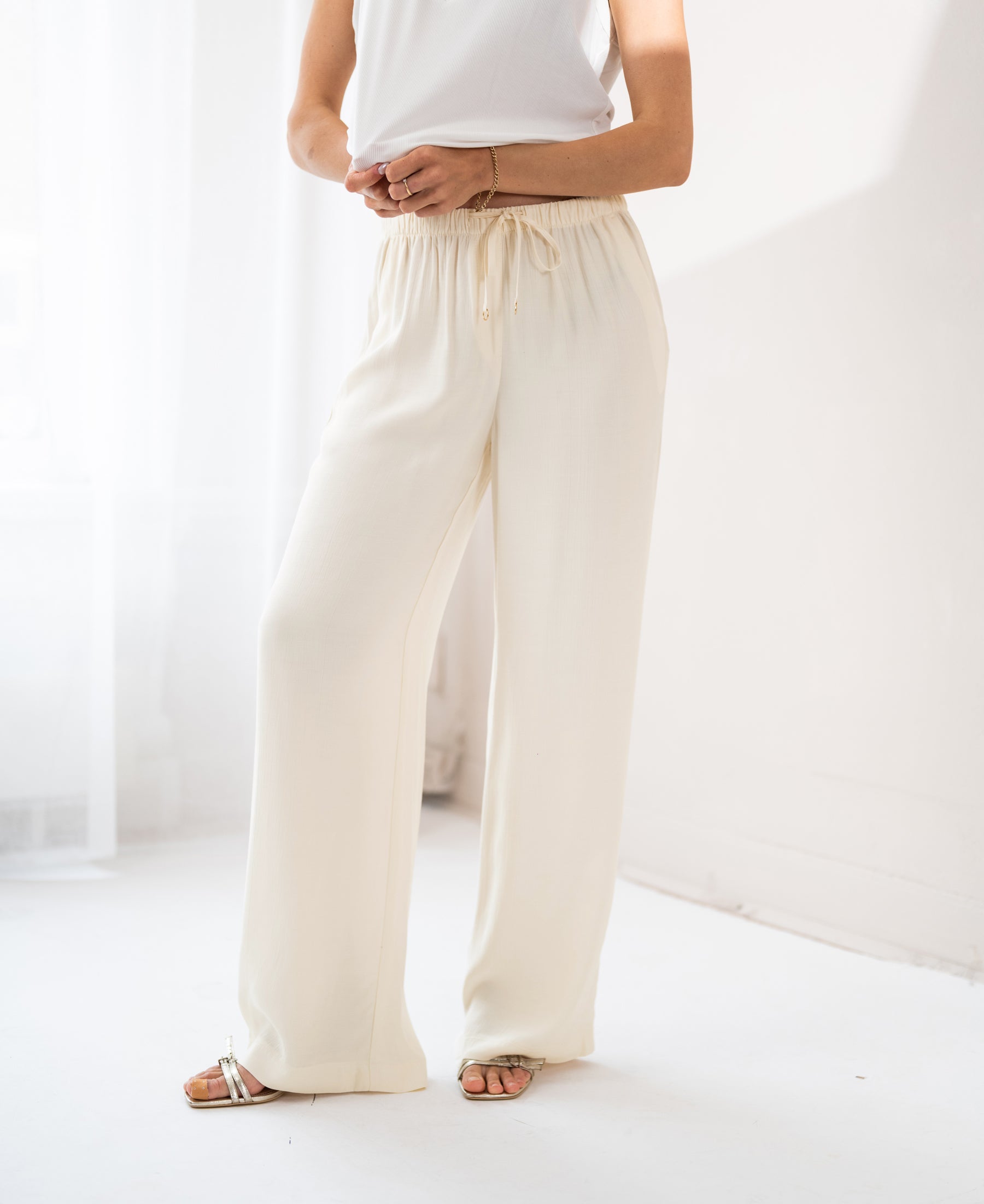 Cream LA LYNETTE trousers by PLEIN PUBLIQUE shown in a bright, minimal room.