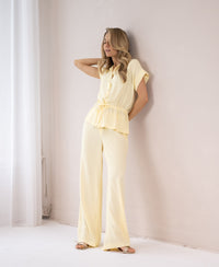Light yellow blouse in soft fabric, shown on a woman standing by a white wall with eyes closed, in gentle lighting.