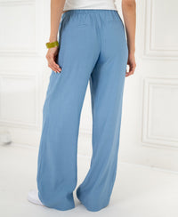 Back view of person wearing LA LYNETTE blue jeans by PLEIN PUBLIQUE, standing against a white wall.