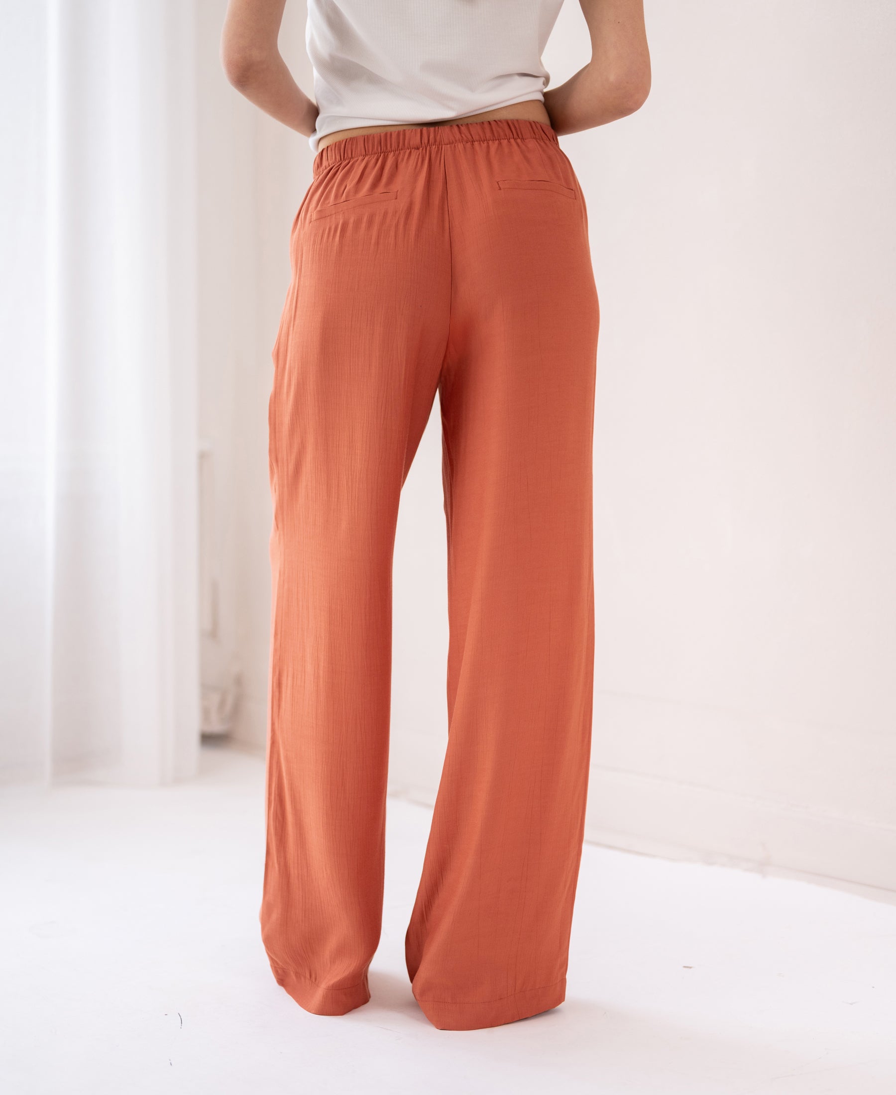 Person wears LA LYNETTE Terra pants in a bright, minimal white room.