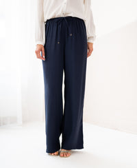 Person wearing dark blue LA LYNETTE trousers by PLEIN PUBLIQUE, standing indoors on a light floor.