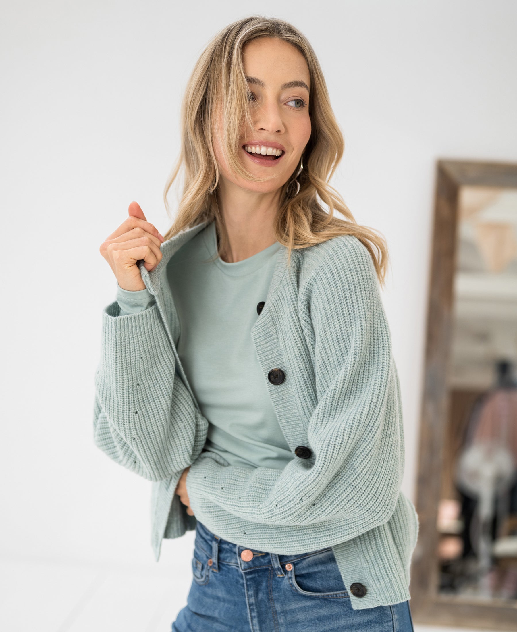 Woman wearing light green Merino wool vest stands indoors.