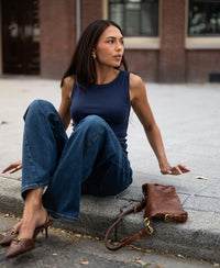 Woman in luxurious and soft dark blue boatneck top sits on curb with a brown handbag.