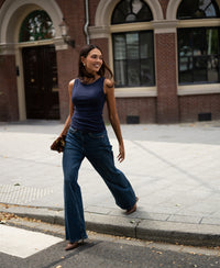 Woman wearing a luxurious and soft dark blue boatneck top, shown walking outdoors and smiling.
