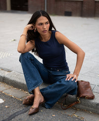 Woman wearing luxe and soft dark blue boat neck top sits curbside on city street.