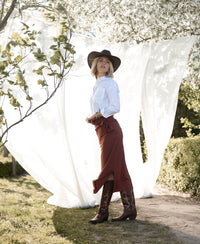 White striped LA PASCALLE blouse displayed against a backdrop of white fabric and greenery.