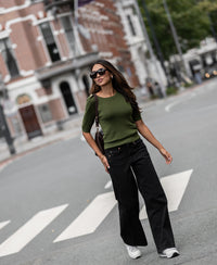Woman wearing an olive green Merino wool LE MAJOR sweater crosses a city crosswalk.