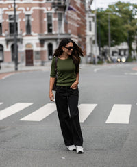Woman wearing olive green Merino wool sweater walks outdoors.