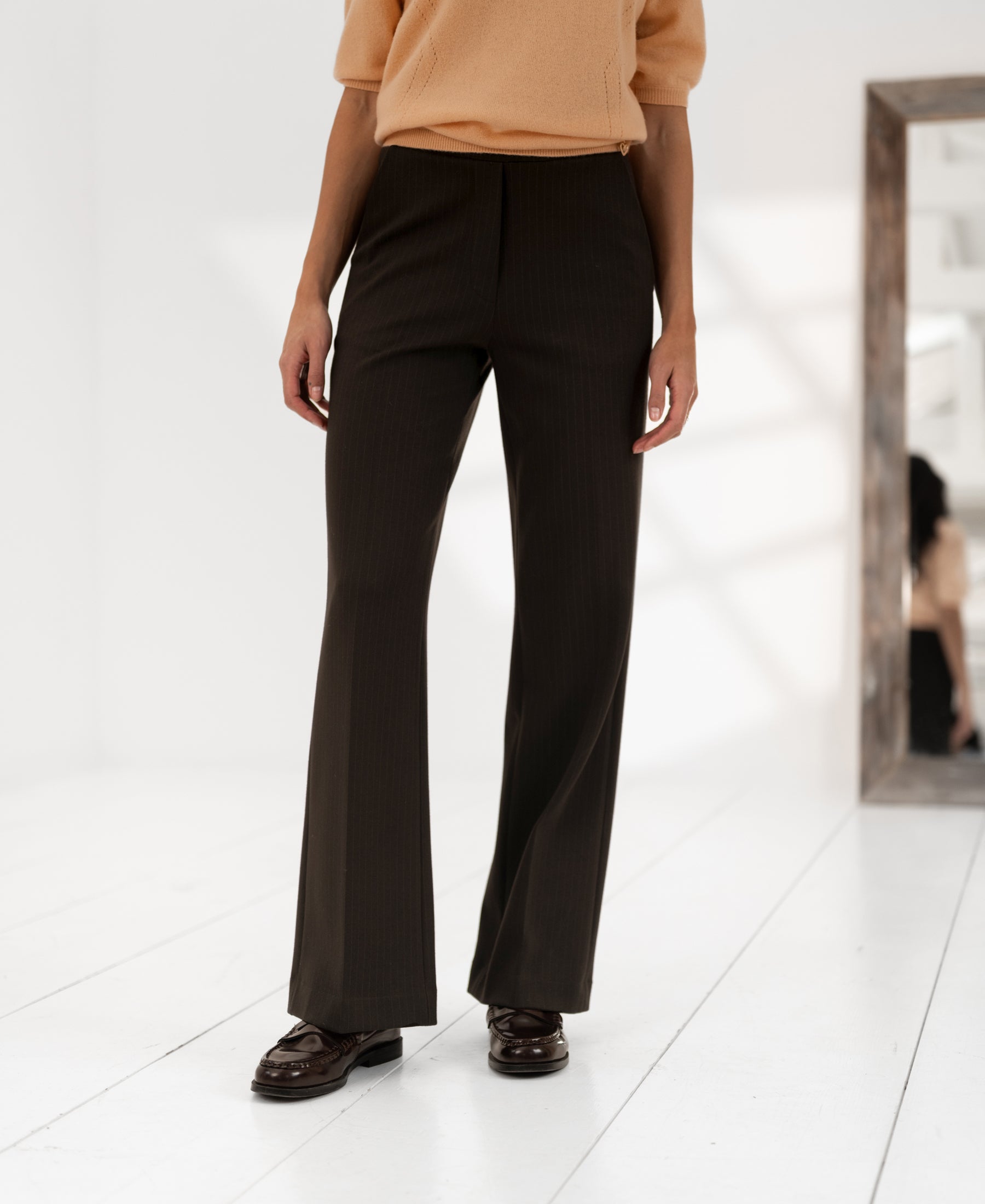 Dark brown pinstripe trousers displayed on a white floor with a mirror.
