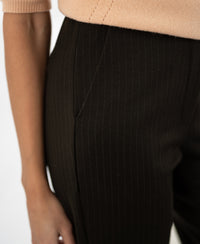 Close-up of a person wearing dark brown pinstripe trousers, arm by their side.