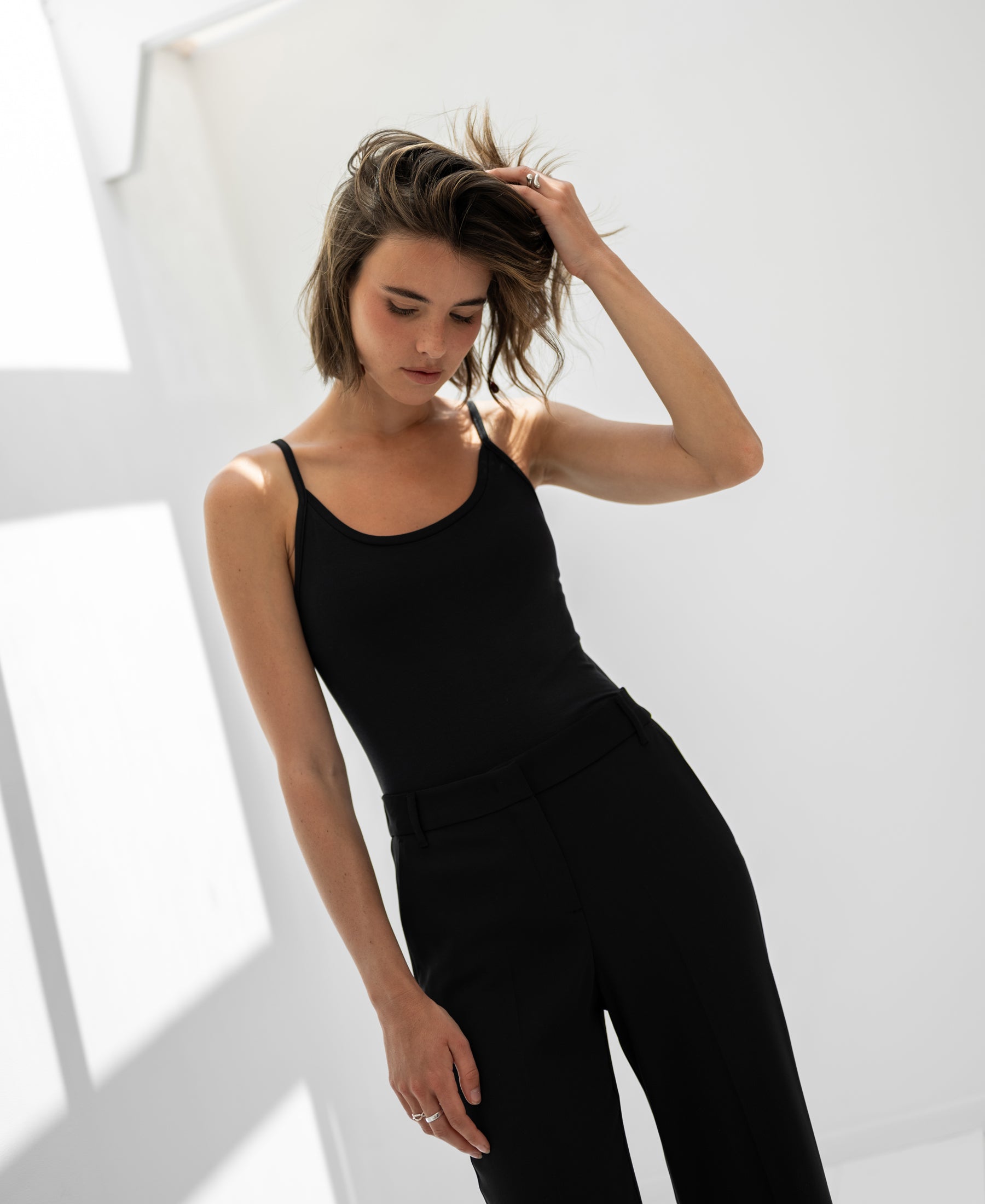 Black PLEIN PUBLIQUE Second Skin Top LE MARAIS displayed indoors with sunlight casting shadows on a white wall.