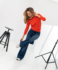 Vrouw poseert binnen in de LA MARCEAU Coral Red merino polo sweater van PLEIN PUBLIQUE.