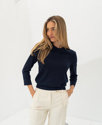 Woman wearing PLEIN PUBLIQUE's dark blue Merino sweater LA MARCEAU in a bright room.