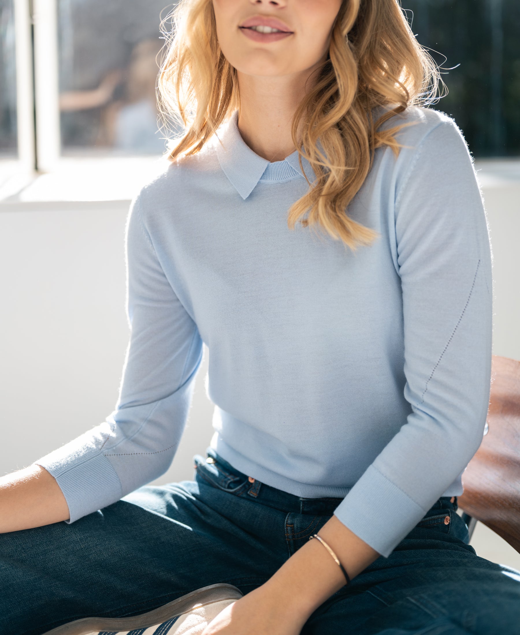 Woman wearing a light blue PLEIN PUBLIQUE Merino sweater with polo collar.