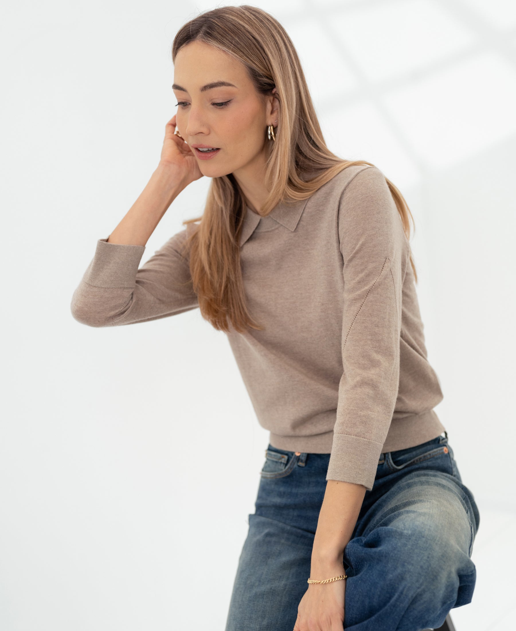 Woman wearing the LA MARCEAU Merino wool polo sweater in Sand from PLEIN PUBLIQUE, seated and looking down.