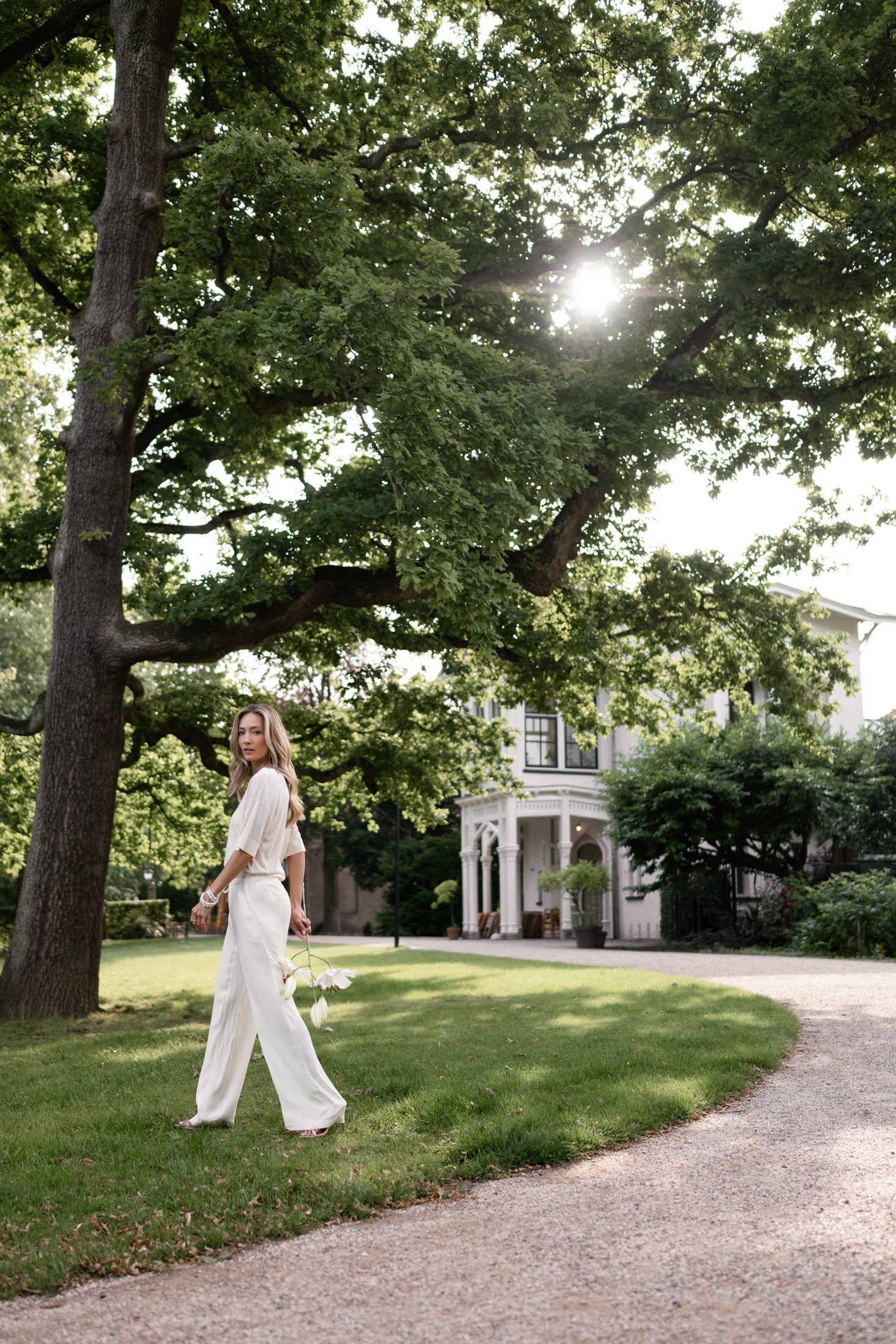 Woman wears cream LA LYNETTE pants, shown walking outdoors.
